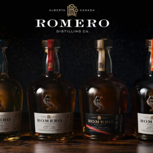 Four bottles of ROMERO Distilling Co. rum from Alberta, Canada: spiced, amber, sherry cask finish and dark, lined up on a dark wooden surface beneath the ROMERO logo