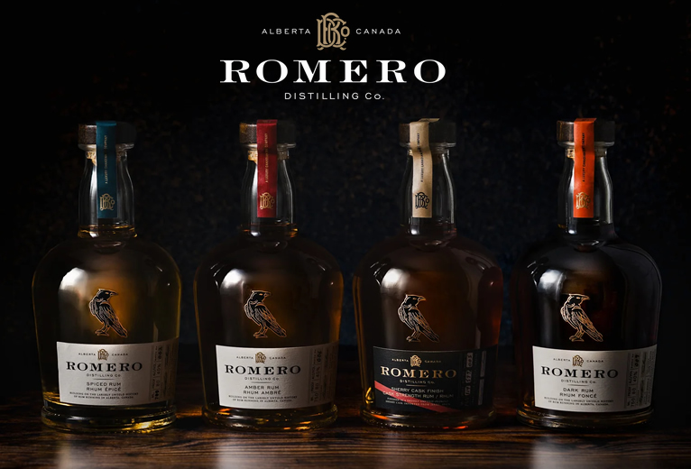 Four bottles of ROMERO Distilling Co. rum from Alberta, Canada: spiced, amber, sherry cask finish and dark, lined up on a dark wooden surface beneath the ROMERO logo